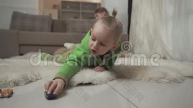 有时髦发型的小男孩和他的玩具车躺在毛茸茸的地毯上。 姐姐在玩泰迪